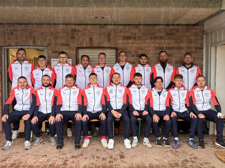 Gruppenshot von 18 Sportlern in einheitlicher Kleidung, im Freien vor einer Backsteinmauer.