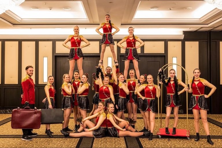 Gruppendarstellung von Tänzern in rot-goldenen Kostümen, mit akrobatischen Posen.