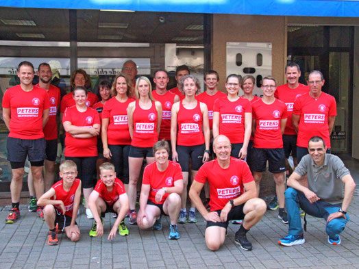 Gruppe von Läufern des FC Keldneich in roten T-Shirts, stehen vor einem Gebäude, lächeln und posieren.