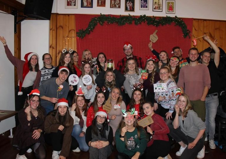 Eine Gruppe von Personen in Weihnachtskleidung feiert zusammen in einem festlichen Raum.